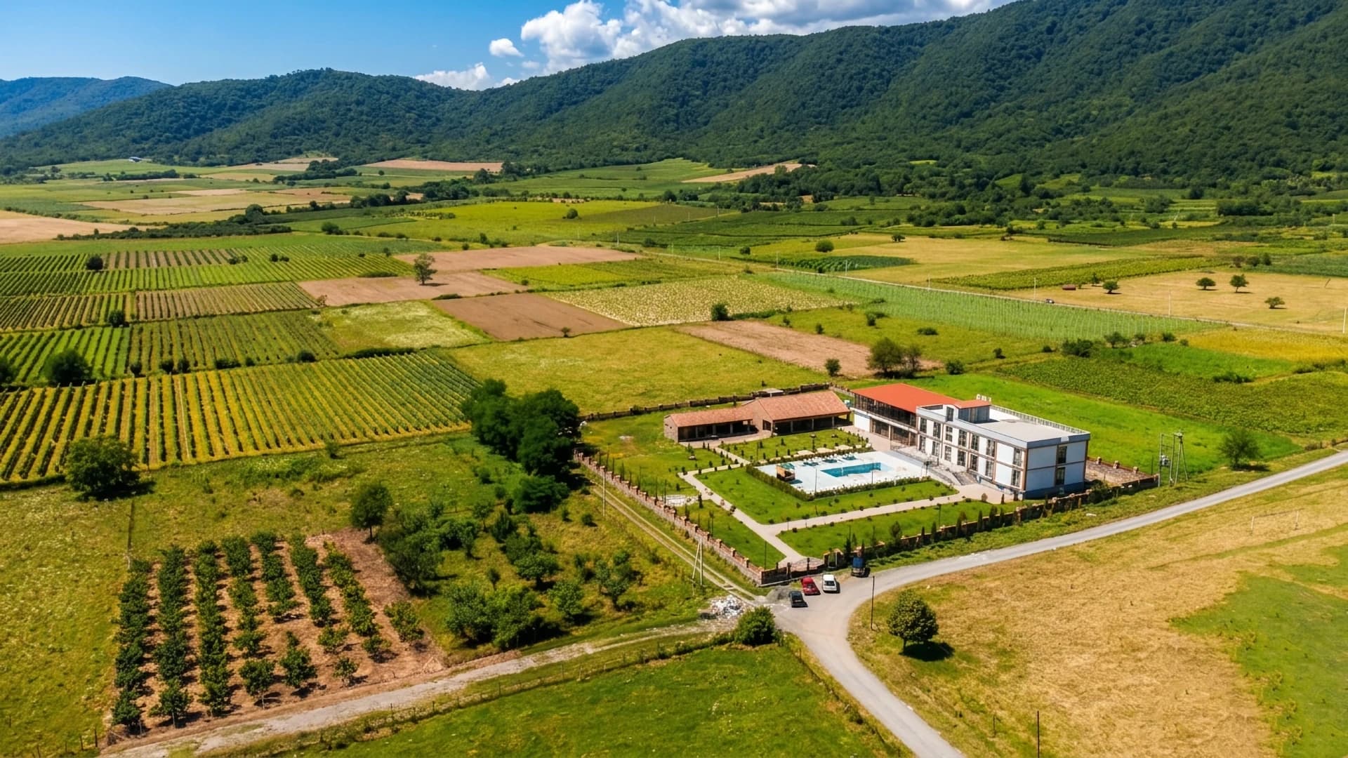 Luftaufnahme des Hotel Inn Gremi zwischen Feldern und Weinbergen vor bewaldeten Hügeln